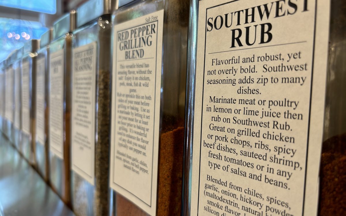 A rack of spice-blend jars in a shop, each with its full printed ingredient label facing out